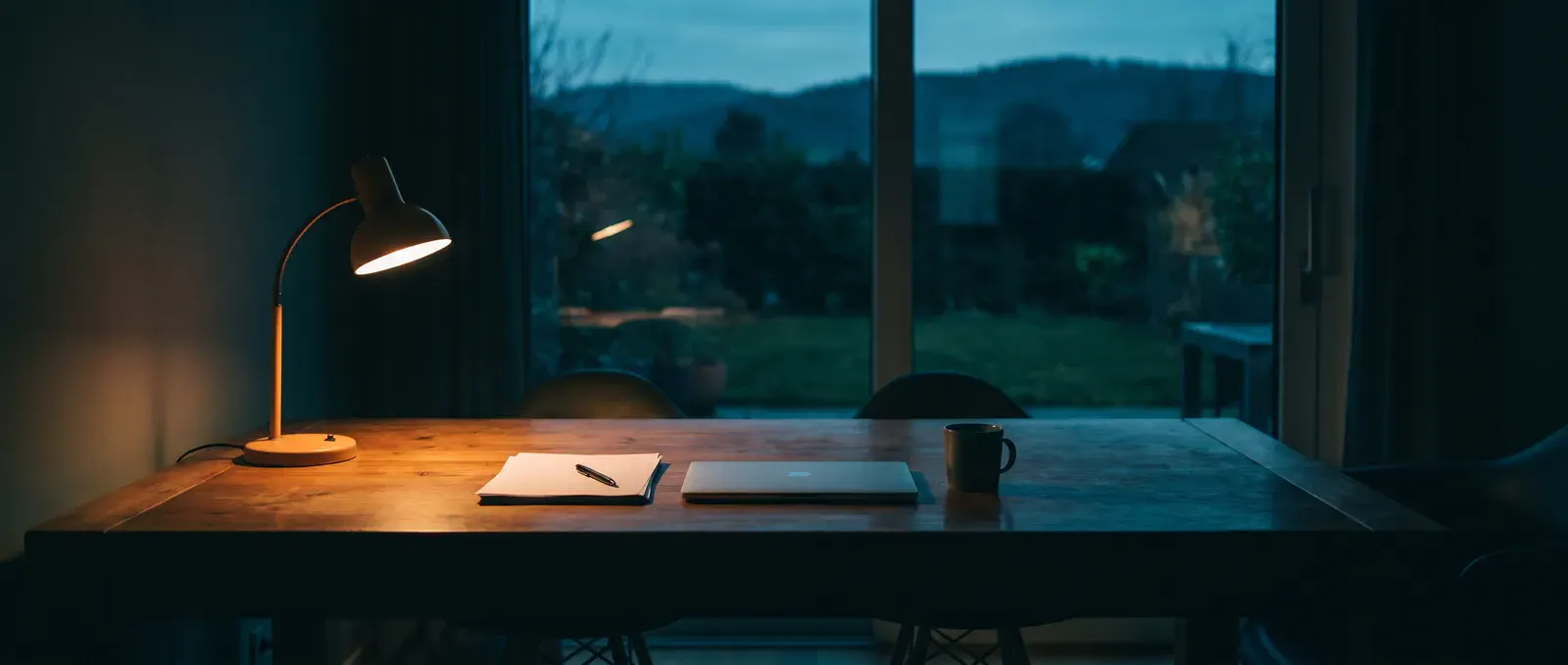 Schreibtisch am Abend mit Laptop, Unterlagen und eingeschalteter Leselampe
